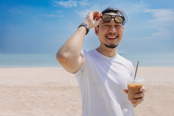 Happy man with hair bun style enjoy the iced coffee walking on the beach.