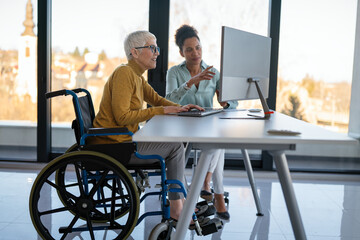 Disabled woman in wheelchair looking at computer, discussing startup project with interracial team