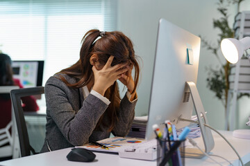 Young professional woman experiencing stress and burnout while working on a computer in a modern office, covering her face with hands and struggling with a difficult task or deadline