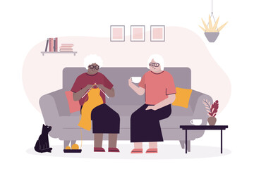 Elderly people spending relaxing day enjoying their hobbies sitting in living room at home knitting, talking and drinking tea. Aged women together,
