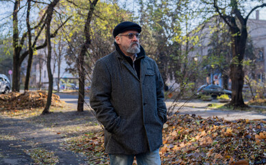 Fototapeta premium Elder grey haired man in the morning outside, man enjoying his morning walk in the city, walking on the street and looking around. Daily routine lifestyle concept.