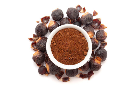 A bowl of Organic Soapnuts or Reetha (Sapindus mukorossi) powder, placed over a heap of Soapnuts berries. Isolated on a white background.