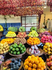 A vibrant fruit market in Funchal with exotic fruits in baskets and dried chilies hanging on the wall, showcasing variety and color.