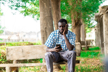 Fototapeta premium image of African American man seated in the garden calmly using phone for leisure, Technology, game, gamer, gaming, connection