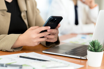 Businesswoman is sitting at her desk using  smartphone to respond to customers
