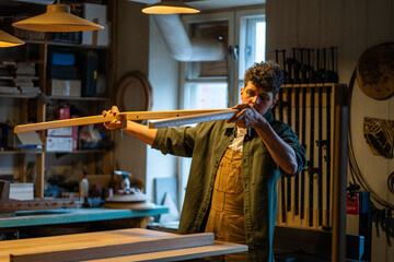 Carpenter inspects table parts legs with ruler for flatness and quality in woodworking workshop....