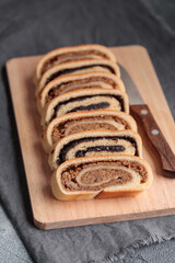 Bejgli, home-baked roll, traditional Hungarian, Eastern European Christmas and Easter sweet bread in slices stuffed with ground walnuts and poppy seed filling on wooden cut board on a gray background