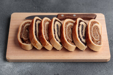 Bejgli, home-baked roll, traditional Hungarian, Eastern European Christmas and Easter sweet bread in slices stuffed with ground walnuts and poppy seed filling on wooden cut board on a gray background
