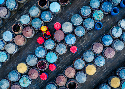 Aerial view of vibrant circles of clay urns and a worker with a yellow hat in a food production scene, Ham Tien, Vietnam.