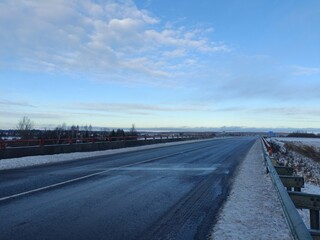 Two way road in countryside. Two lane street. Trees and bushes growing around. Snow is laying on ground. Countryside.