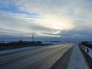 Two way road in countryside. Two lane street. Trees and bushes growing around. Snow is laying on ground. Countryside.