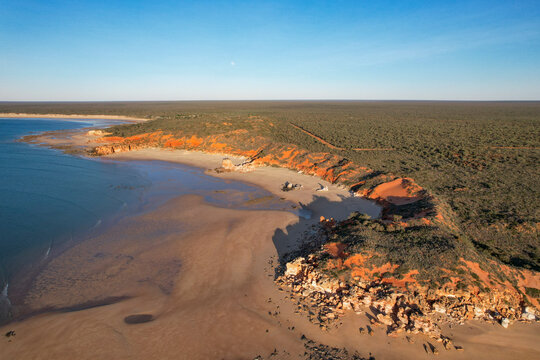 Aerial view of echo beach resort coastline with ochre cliff and the moon, Lagrange, Western Australia.