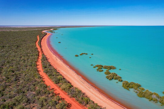 Aerial view of red sand beach and turquoise water with mangroves along the coastline, Broome, Australia.