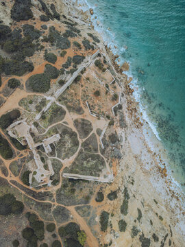 Aerial view of the historic ruins of Forte de Almadena on a rocky cliff overlooking the turquoise ocean, Budens, Portugal.
