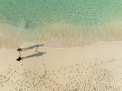 Aerial view of people walking on a sandy beach with clear water and waves, North Eleuthera, The Bahamas.