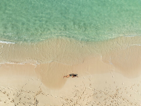 Aerial view of a woman relaxing on a beautiful beach with turquoise clear water and soft sand, North Eleuthera, The Bahamas.