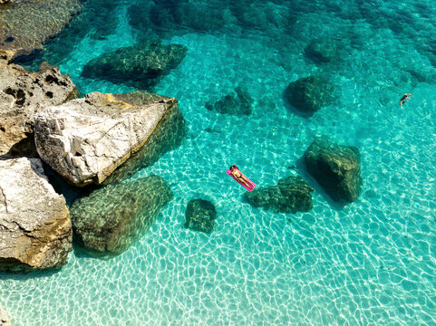 Aerial view of mariolu beach with a woman on an inflatable mattress in turquoise water, Baunei, Italy.