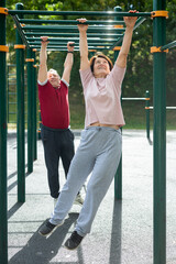 Fototapeta premium Married couple at retirement age goes in for sports on sports ground - with the help of hands they move along horizontal ladder