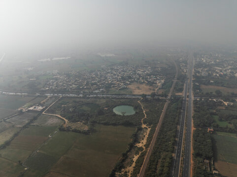 Aerial view of expansive expressway surrounded by serene fields and a tranquil village, Fatehpur Sikri, India.