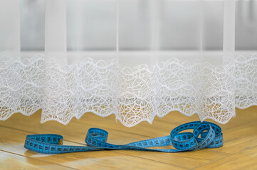 Obraz premium Centymetr krawiecki leżący obok wiszącej w oknie firance, 