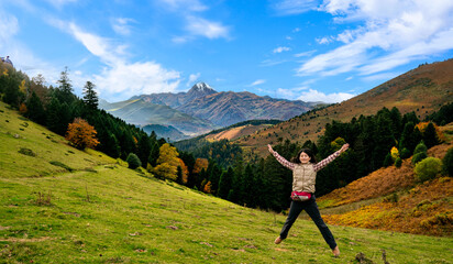 A joyful moment in the Pyrenees with Pic du Midi d’Ossau towering majestically in the background, surrounded by vibrant autumnal valleys and lush forests.