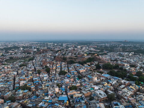 Aerial view of the dense cityscape with traditional blue buildings and rooftops at sunset, Jodhpur, India.