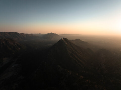 Aerial view of the majestic Shree Savitri Mata Temple surrounded by serene mountains and a tranquil valley at sunset, Pushkar, Rajasthan, India.