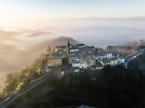 Aerial view of a serene village enveloped in fog and mist at sunrise with rolling hills, Piantravigne, Italy.