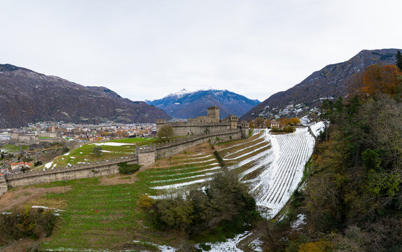 Aerial view of the historic Castle of Montebello surrounded by snow-capped mountains and vineyards, Bellinzona, Switzerland.