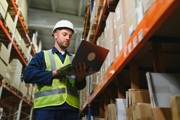 Warehouseman checking delivery, stock in warehouse on laptop. Warehouse manager using warehouse...