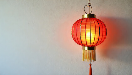 Fototapeta premium A vibrant image of a round Chinese lantern with a detailed tassel, glowing softly, set against a plain white background.