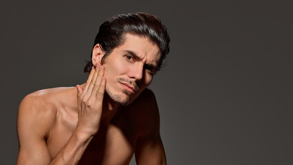 Obraz premium Man looking upward slightly, shows soft smile against dark background. His posture and sleek hairstyle suggest ease and confidence. Concept of male beauty and facial care, anti-aging procedures.