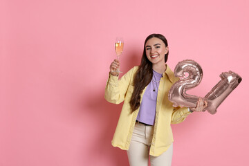 Coming of age party - 21st birthday. Happy young woman with number shaped balloons and glass of sparkling wine on pink background, space for text