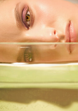 Close up of a young woman face lying behind a glass container
