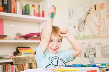 Smiling boy holding coloring pens above his head
