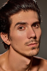 Fototapeta premium Close-up of man with neutral expression gazing slightly off-camera against dark background. Male model with slicked-back hair and sharp facial features. Concept of male beauty and facial care,