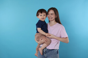 Happy mother with her cute little son on light blue background