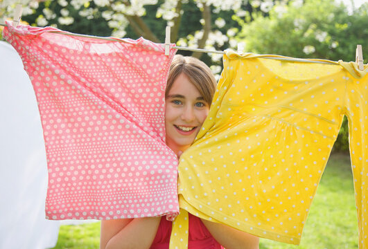 Smiling teenaged girl poking her face between two t-shirts hanging from a clothesline
