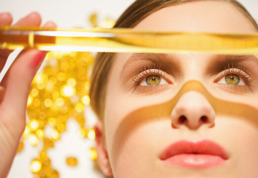 Close up of a young woman face holding a golden glass tube over her face
