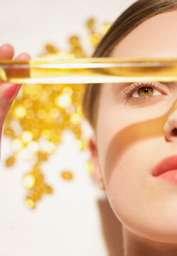 Close up of a young woman face holding a golden glass tube over her face
