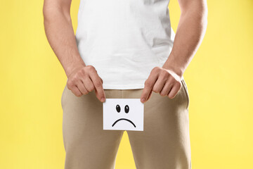 STD (sexually transmitted diseases). Man holding sticky note with drawn sad face on yellow...