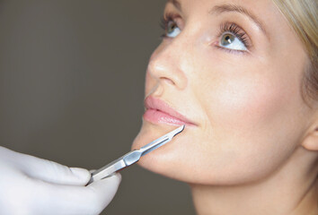 Doctor's Hand Holding Surgical Scalpel in front of Woman's Face
