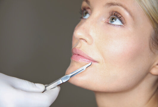 Doctor's Hand Holding Surgical Scalpel in front of Woman's Face
