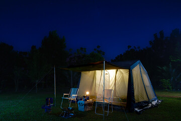 Camping tents at night, vintage cabin tents, antique gas lamps, retro chairs, and a group of camping tents with outdoor coffee-making facilities on  tables in a forest camping area in the forest