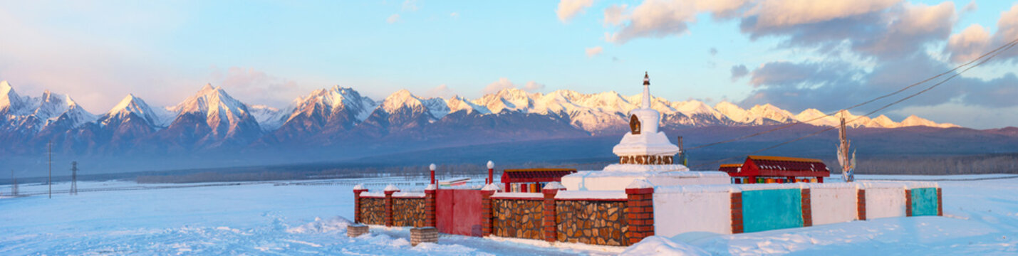 Panoramoc view of Buddhist stupa against the background of the snowy Eastern Sayan Mountains at winter sunset. Siberia. Baikal region. Buryatia. Tunka foothill valley