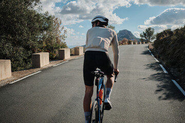 Naklejka premium Cyclist rides road bike on scenic mountain road. Epic view, sunny day. Active lifestyle, adventure, freedom concept. Perfect for travel, sports, or health publications.
