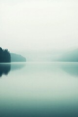 Fototapeta premium A serene misty lake surrounded by trees and mountains.