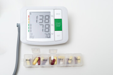 Digital blood pressure monitor showing high blood pressure with daily pill organizer