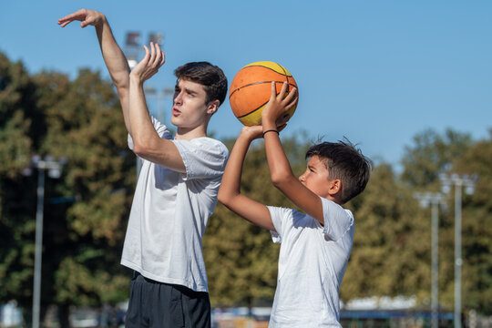 Outdoor basketball training for kids, featuring a coach teaching a young boy shooting technique. Focus on skill building, precision, and fostering youth development in sports.