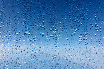 Close-Up of Water Droplets on Glass Surface Against Blue Sky Background for Abstract and Nature Themes